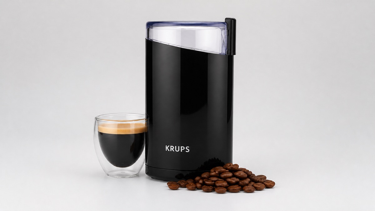 Black Krups coffee grinder with a glass of espresso and coffee beans